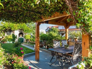 Ein Terrassenbereich im Freien mit einer Pergola, Sitzgelegenheiten und Topfpflanzen.