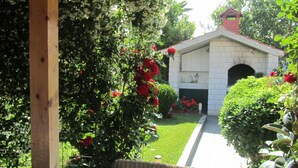 Un patio couvert avec un fauteuil en osier, une cheminée en briques et un jardin où poussent des roses rouges.