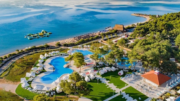 Une vue aérienne d’un complexe hôtelier doté d’une grande piscine centrale, de plusieurs petites piscines et d’une zone de plage.