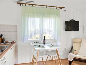 A modern kitchen with a dining area, a TV mounted on the wall, and a view of the outdoors through a window with sheer curtains. - Appartement mit Balkon by Interhome (Šibenik)