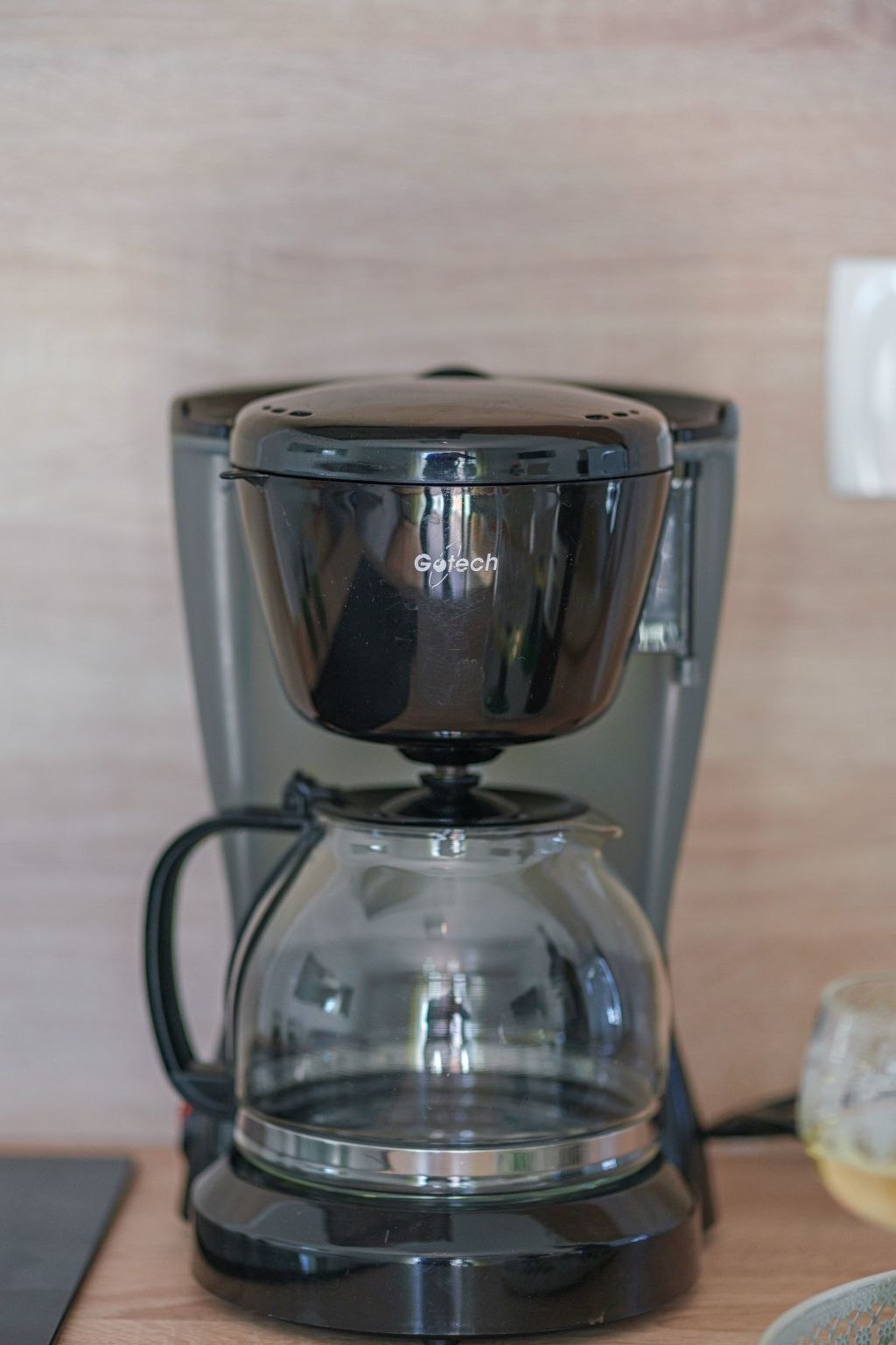 A coffee maker with a transparent water reservoir and a black base, placed on a wooden surface.