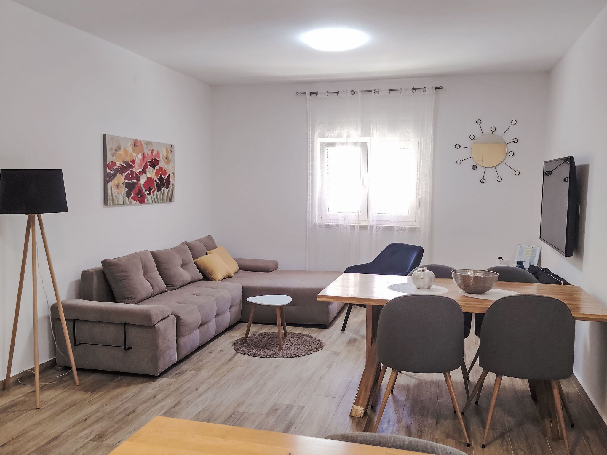Un salon moderne comprenant un canapé, une table à manger avec des chaises, un lampadaire, un tableau, une fenêtre avec des rideaux et une horloge murale.