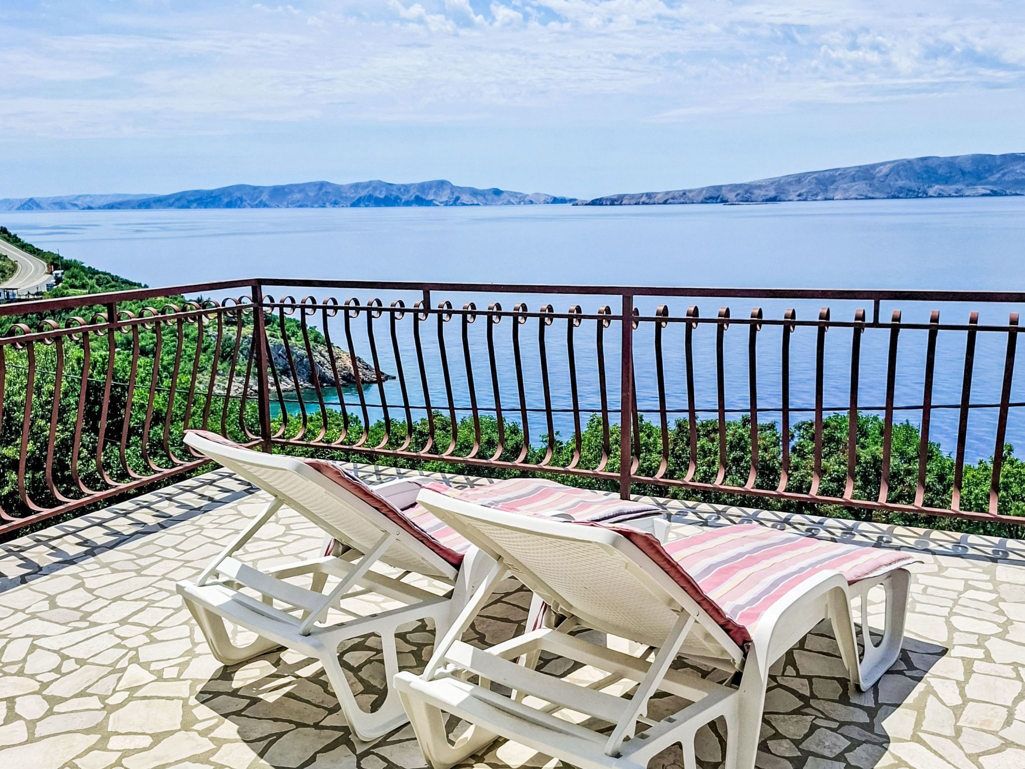 Un balcón con dos sillones blancos y una mesa con diseño, que ofrece vistas panorámicas de una masa de agua y montañas a lo lejos.