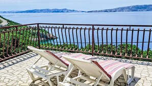 Een balkon met twee witte loungestoelen en een tafel met een patroon, met uitzicht op een schilderachtig wateroppervlak en verre bergen.