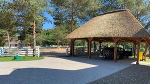 Ein überdachter Pavillon mit einem Reetdach, Kieswegen und einem eingezäunten Bereich mit Bäumen und einem Gebäude im Hintergrund.