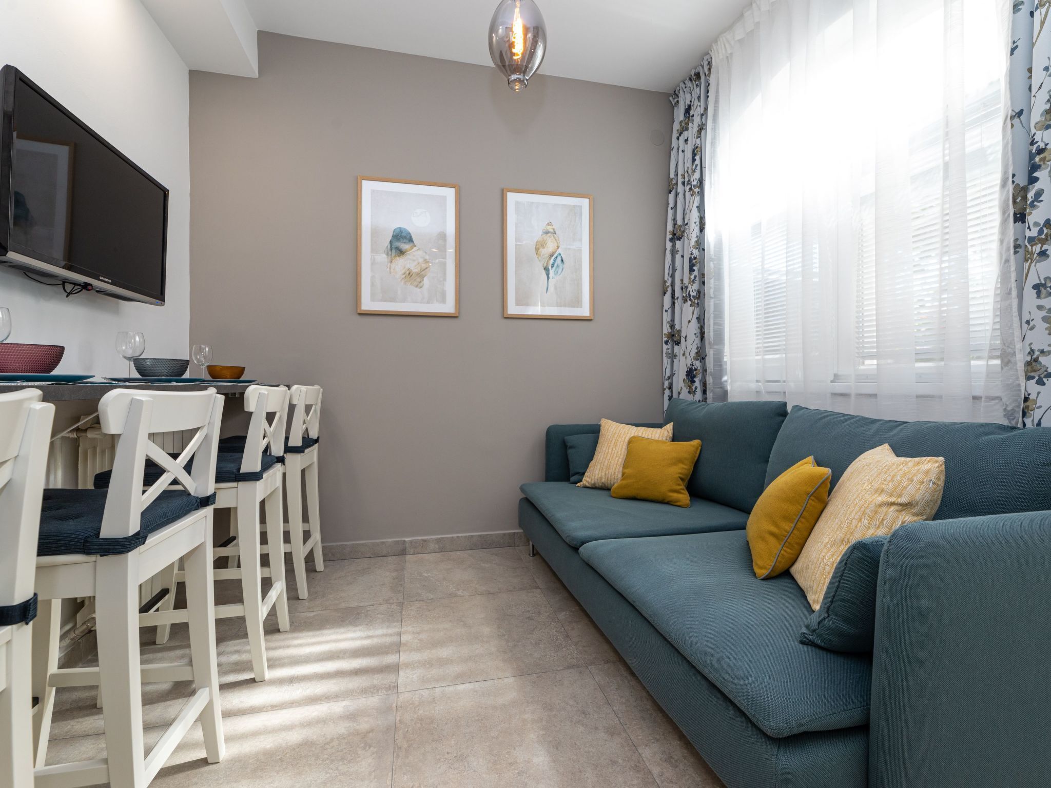 A modern living room with a teal sofa, white chairs, a flat-screen TV, and two framed artworks on the wall.