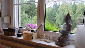 A window with a statue of a seated figure holding a cup, a small basket, and a candle holder on the windowsill. - am Wald mit Sauna by Interhome (Bad Elster)
