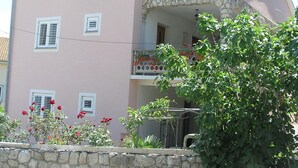 A two-story building with a pink facade, stone accents, and a balcony with a railing. - Zwei-Zimmer-Wohnung Radosav by Interhome (Krk/Šilo)