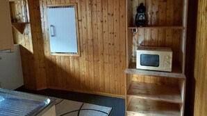 A wooden-paneled room with a window, a microwave, and a shelf with a kettle and a coffee maker. - Wärschu by Interhome (Albinen)