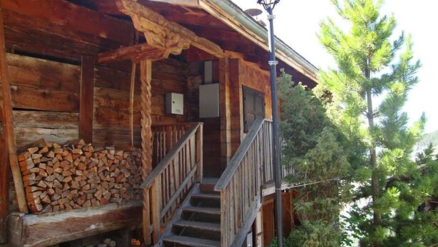 A rustic cabin with a wooden exterior, a porch with a stack of firewood, and a staircase leading to the entrance. - Wärschu by Interhome (Albinen)
