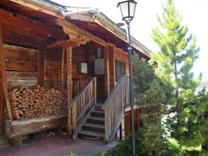 A rustic cabin with a wooden exterior, a porch with a stack of firewood, and a staircase leading to the entrance. - Wärschu by Interhome (Albinen)