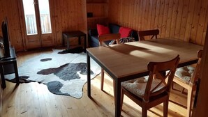 A wooden cabin interior with a dining table, chairs, a television, a cowhide rug, and a window with a view. - Wärschu by Interhome (Albinen)