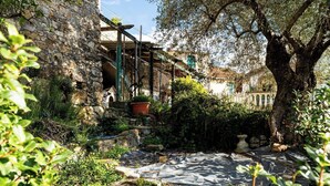 Un edificio de piedra con un jardín rústico, un árbol y un camino.