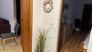 En stue med en trædør, en rød sofa, en grå lænestol, et skab og en potteplante.