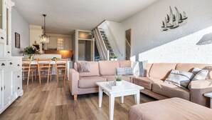 A modern living room with a sofa, coffee table, and dining area. - Lovely apartment for 4 guests with WIFI, pool, TV, terrace and pets allowed (Bruinisse)