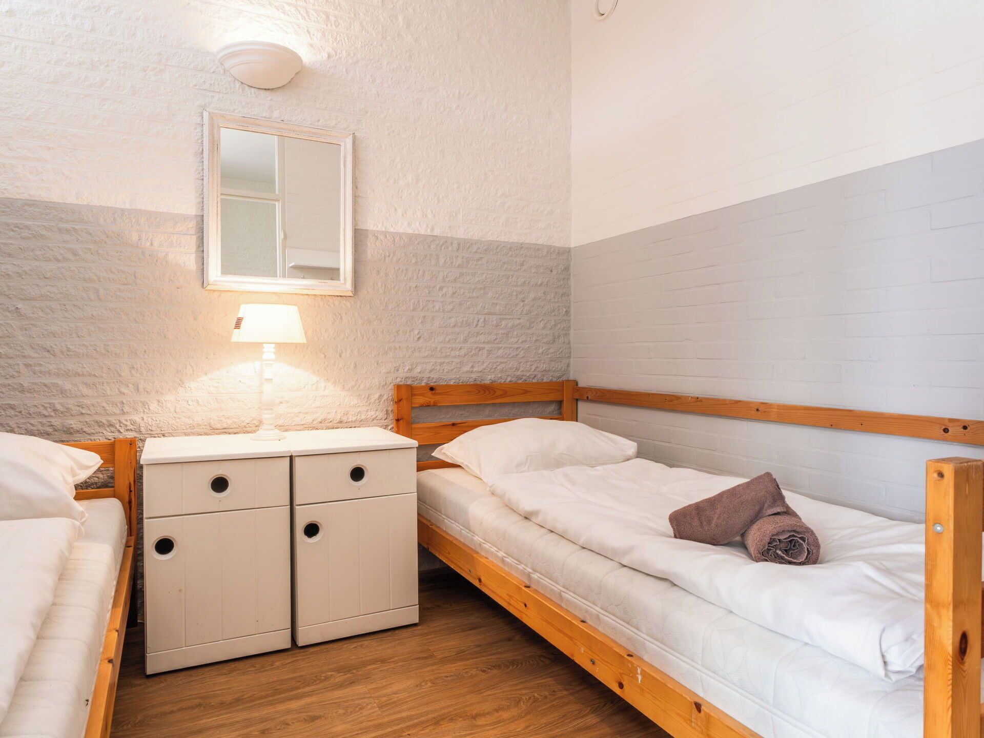 Una habitación pequeña y acogedora con una cama litera, una mesita de noche con una lámpara y un espejo en la pared.
