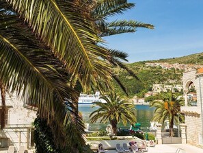 Vista sulla costa con palme, cielo azzurro limpido e un edificio storico con un arco.