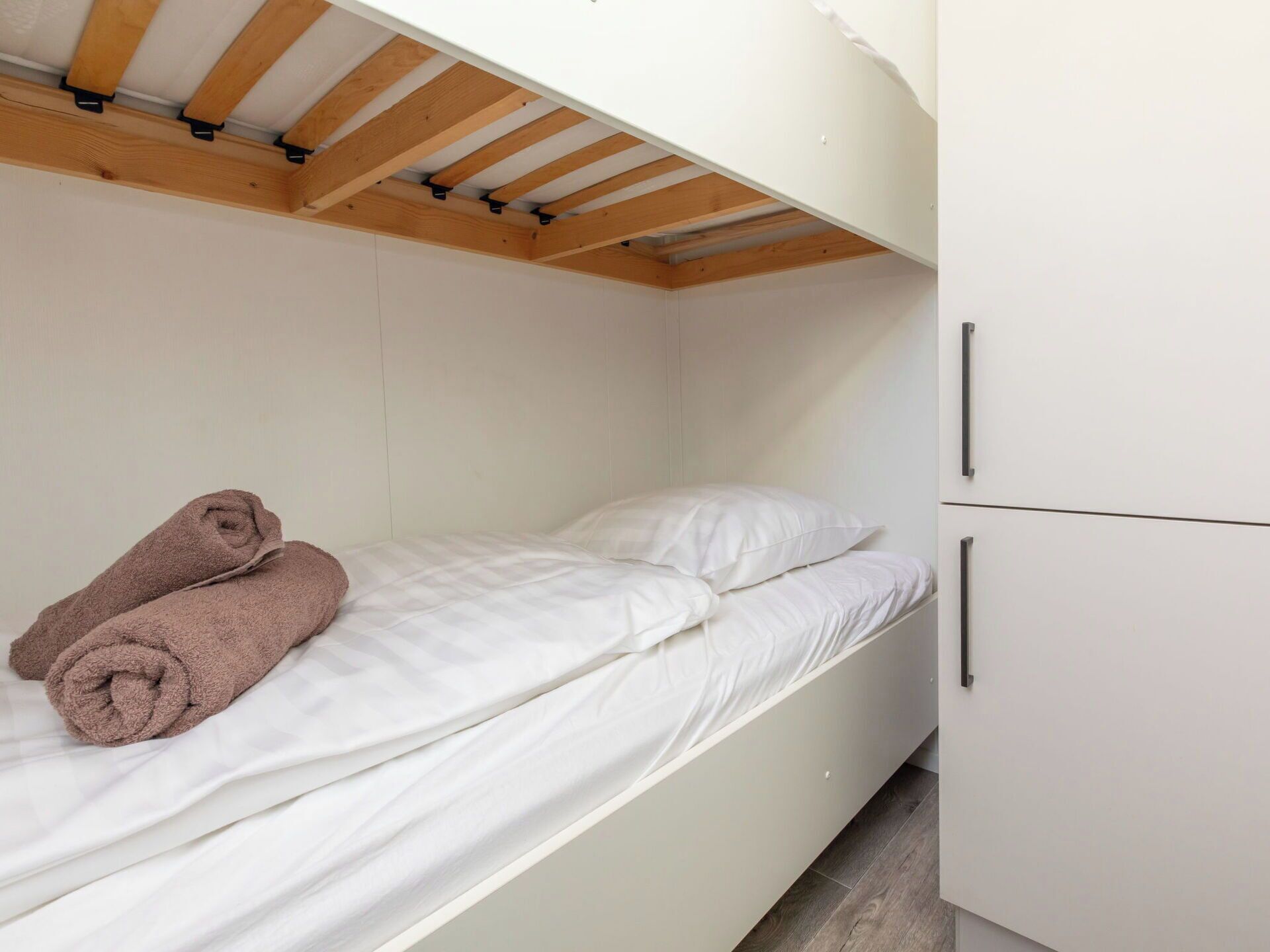 Una cama individual con ropa de cama blanca y dos almohadas, techo de madera y un armario blanco de dos puertas.