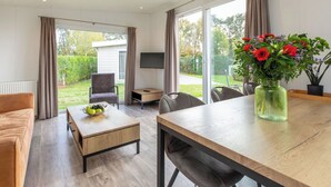 Ett modernt rum med ett matbord, stolar, en soffa, en tv och ett stort fönster med gardiner.
