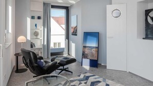 A modern living room with a glass coffee table, a black leather sofa, and a large window with a view of a building. - Stormy im Nauticum by Interhome (Ostseebad Lubmin)