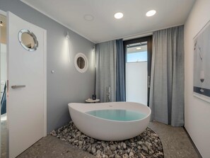 Een moderne badkamer met een vrijstaand bad, een ronde spiegel en een klein tafeltje met een kaars.
