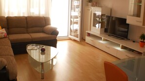 Un salon comprenant un canapé, une table basse en verre, un téléviseur posé sur un meuble et une porte-fenêtre coulissante donnant sur un balcon.
