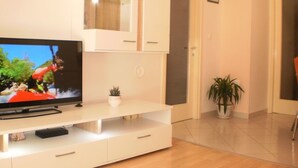 Un salon moderne doté d’un téléviseur à écran plat, de meubles blancs, d’une petite plante et d’une porte donnant sur une autre pièce.