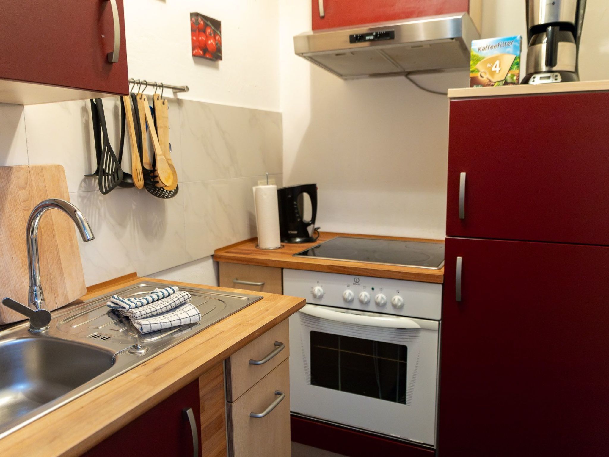 Eine Küche mit Spüle aus Edelstahl, einer Holz Arbeitsplatte und einem Herd. Es hängen Utensilien an der Wand und ein Kaffeeautomat steht auf der Arbeitsplatte.