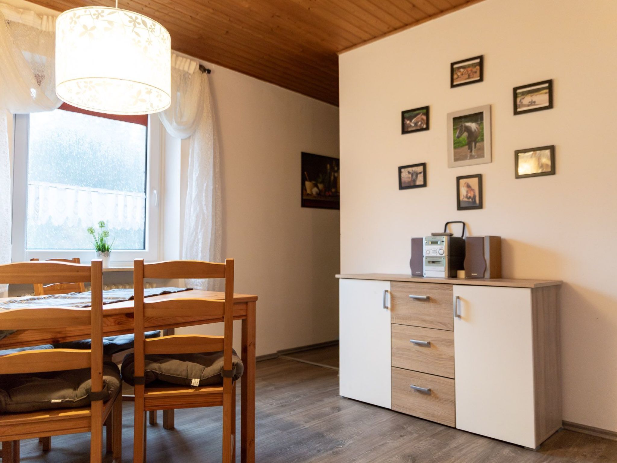 A room with a wooden dining table, chairs, a white cabinet with drawers, and a window with curtains.