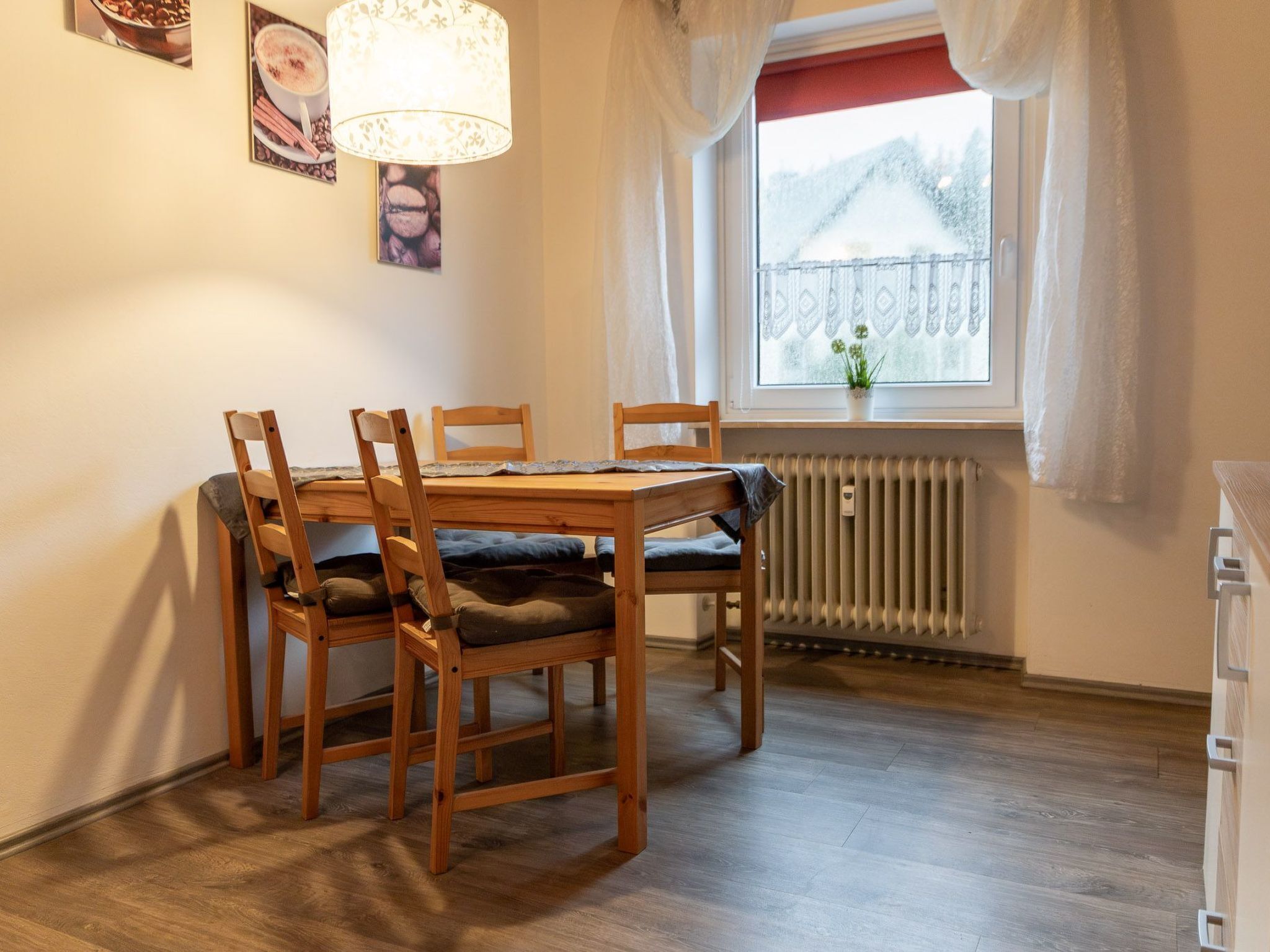 Un coin repas avec une table et des chaises en bois, un radiateur placé sous la fenêtre et une vue sur un paysage enneigé.