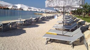 A beach with sun loungers and umbrellas, a pool, and a clear sky. - Carpe Diem by Interhome (Trogir)