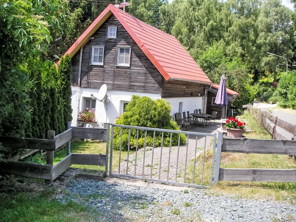 Una casa de madera rústica con techo rojo, antena parabólica y entrada protegida por una reja.
