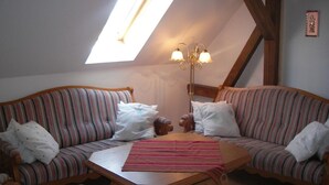 A cozy loft bedroom with a sloped ceiling, a skylight, a wooden table, two striped sofas, and a chandelier.