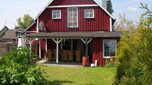 A red two-story house with a covered patio and a fenced yard.