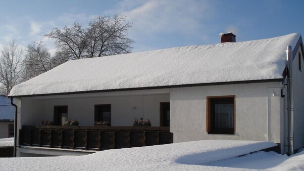 Une maison à deux étages, dont le toit est recouvert de neige, et qui possède un balcon orné de plantes en pot.