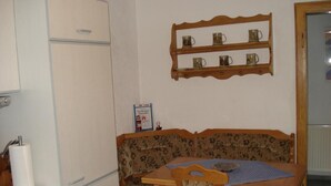 Un coin repas avec une table en bois, un banc orné de motifs floraux et une étagère où sont posées des tasses.