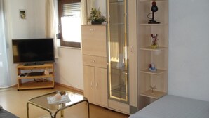 Une pièce comprenant un téléviseur posé sur un meuble en bois, une vitrine avec des étagères, un lit et une petite table avec une lampe.