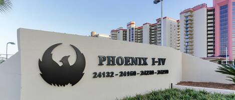 A sign for Phoenix I-IV with a bird logo, surrounded by modern buildings.