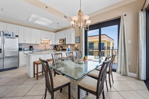 A modern kitchen with white cabinets, a glass dining table, and a large window with a view of a building. - Phoenix III 3159 (Orange Beach)