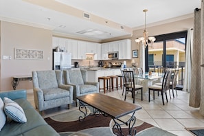A spacious living area with a dining table, two patterned armchairs, a sofa, and a kitchen in the background. - Phoenix III 3159 (Orange Beach)