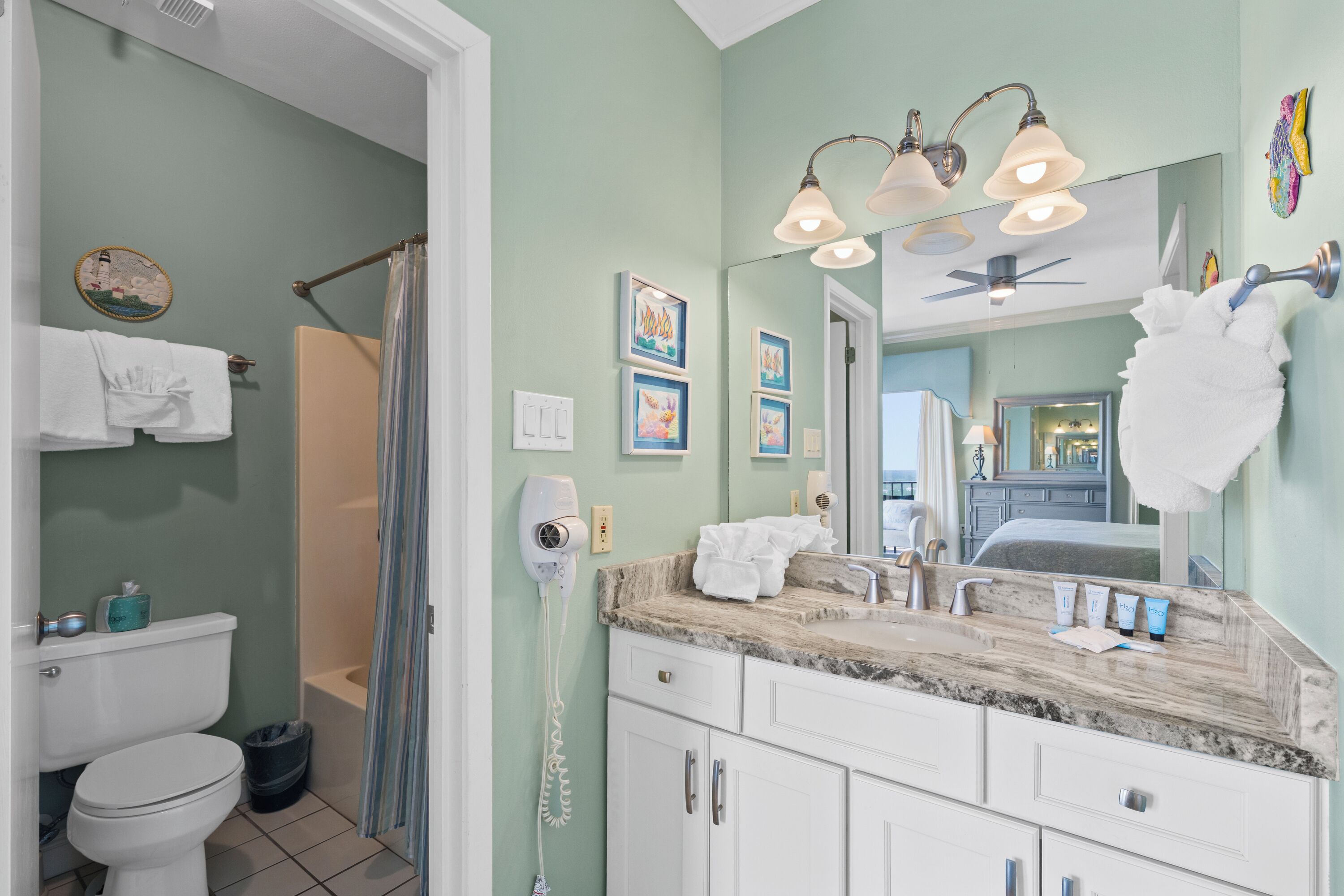 A bathroom with a toilet, sink, and shower. There are towels hanging on the wall, a hairdryer, and framed pictures.