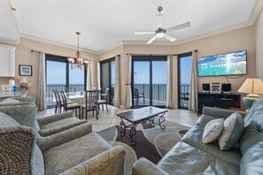 A spacious living area with a balcony, a dining set, and a television displaying 'hosteeva'. - Phoenix III 3159 (Orange Beach)