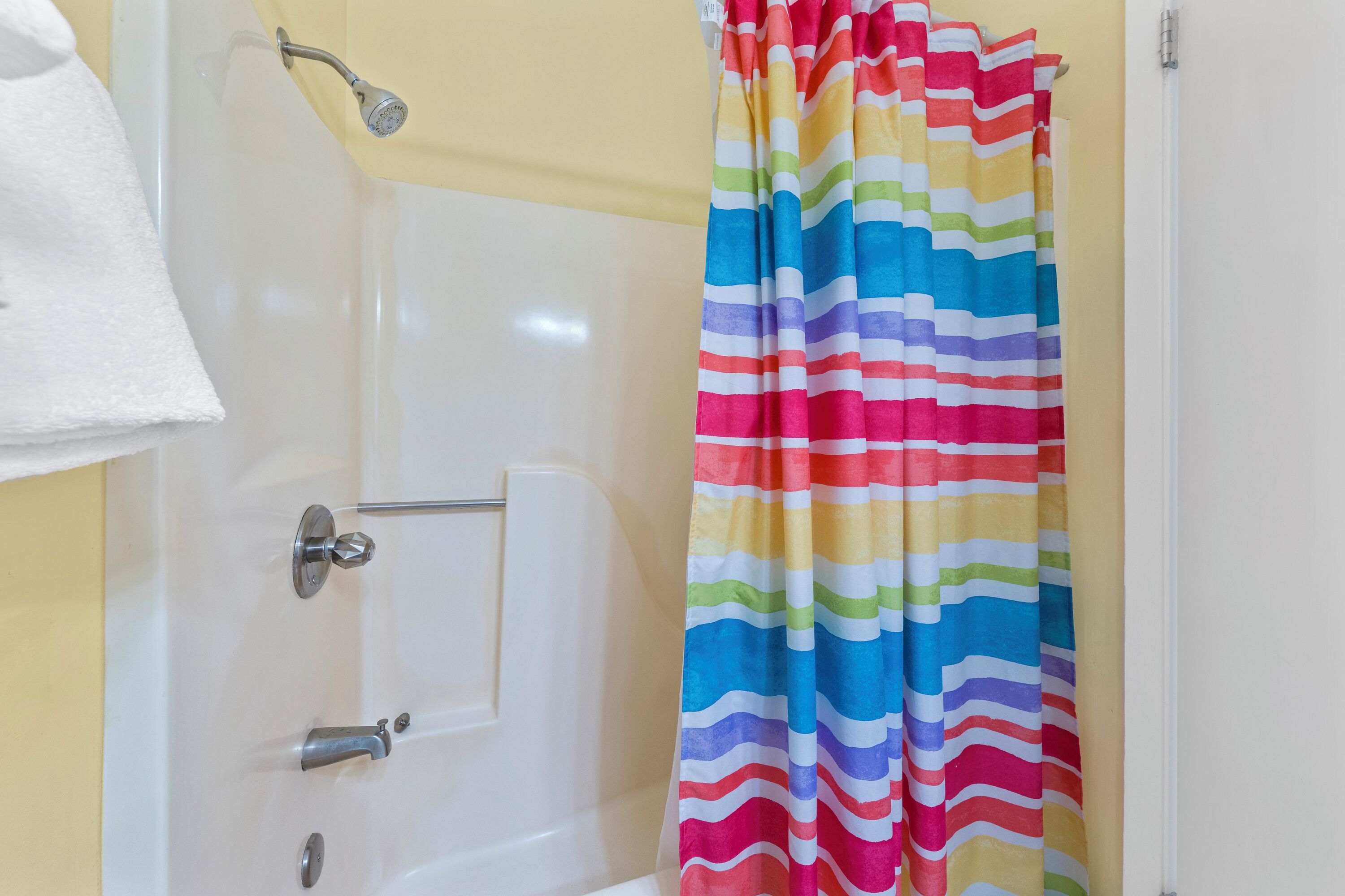 Un baño con una bañera blanca, ducha con cabezal de ducha manual y cortina de ducha a rayas coloridas.