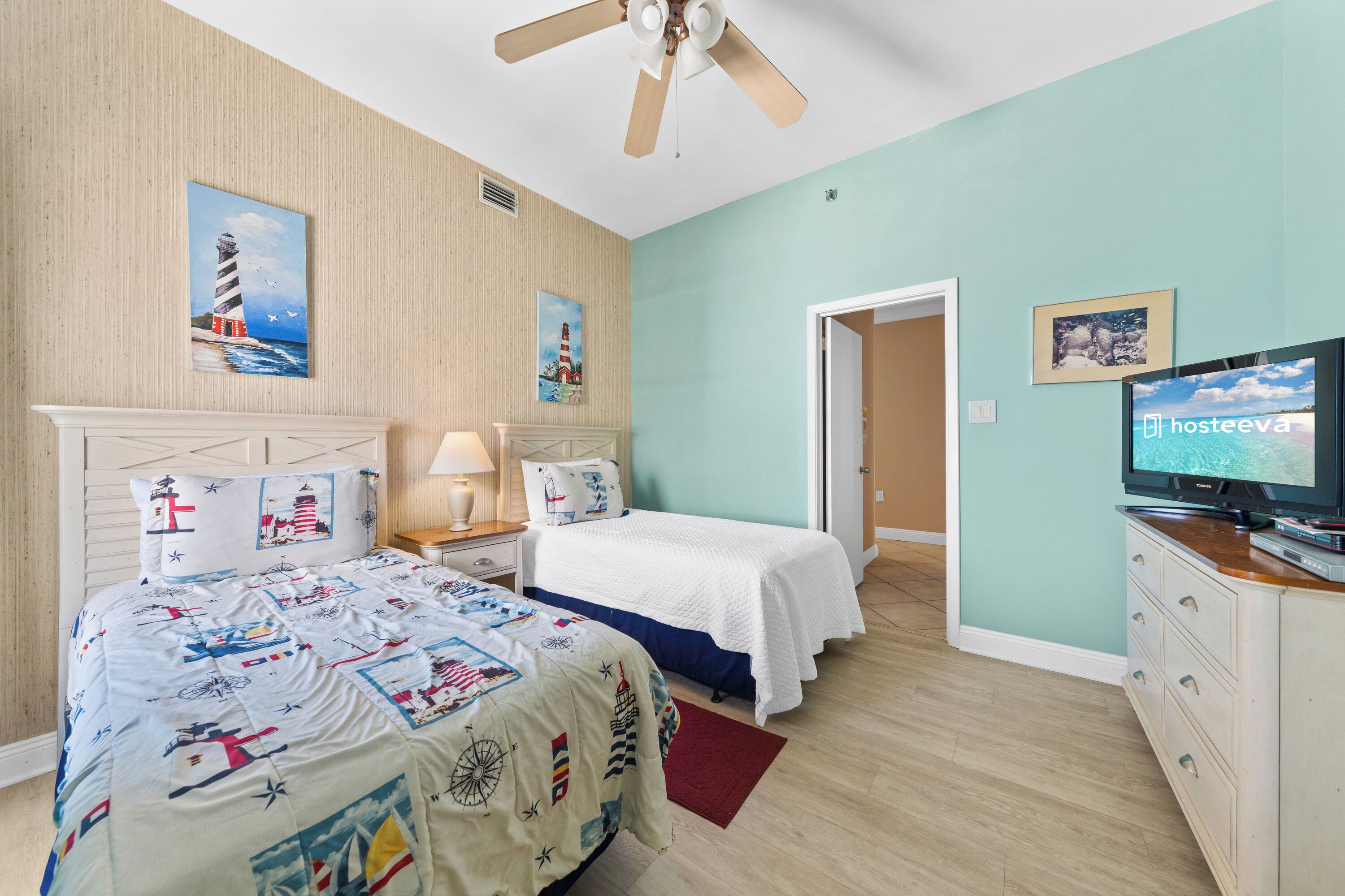 Une chambre à coucher comprenant un lit, un téléviseur, un ventilateur de plafond et une porte donnant sur une autre pièce.