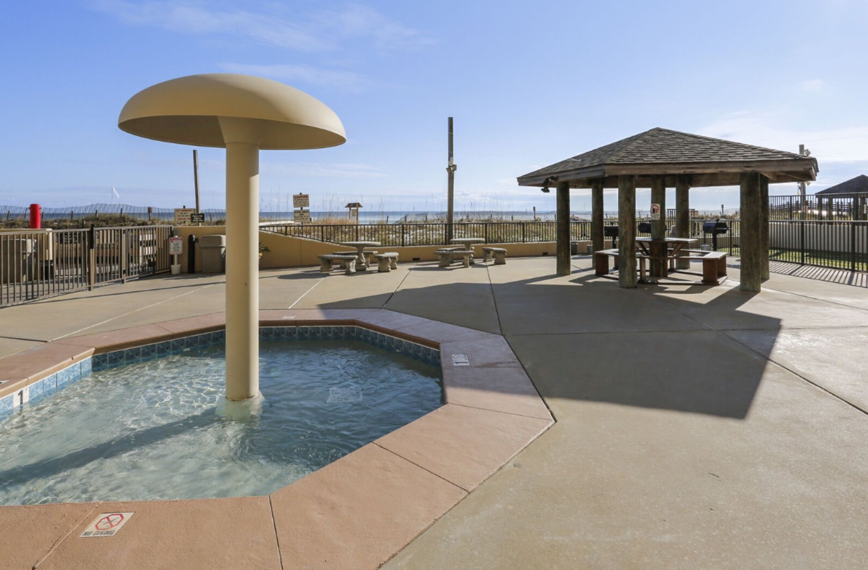 A pool area with a hot tub, picnic tables, and a gazebo.
