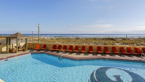 Zona de piscina con vista a la playa, sillas de descanso y un pequeño pabellón.