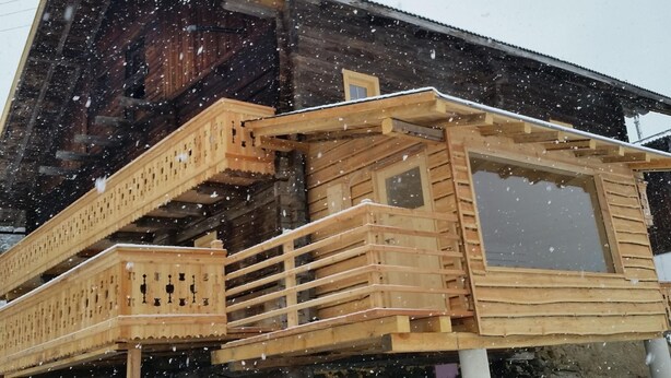 Une cabane en bois dotée d’un balcon et d’une grande fenêtre, entourée de neige.