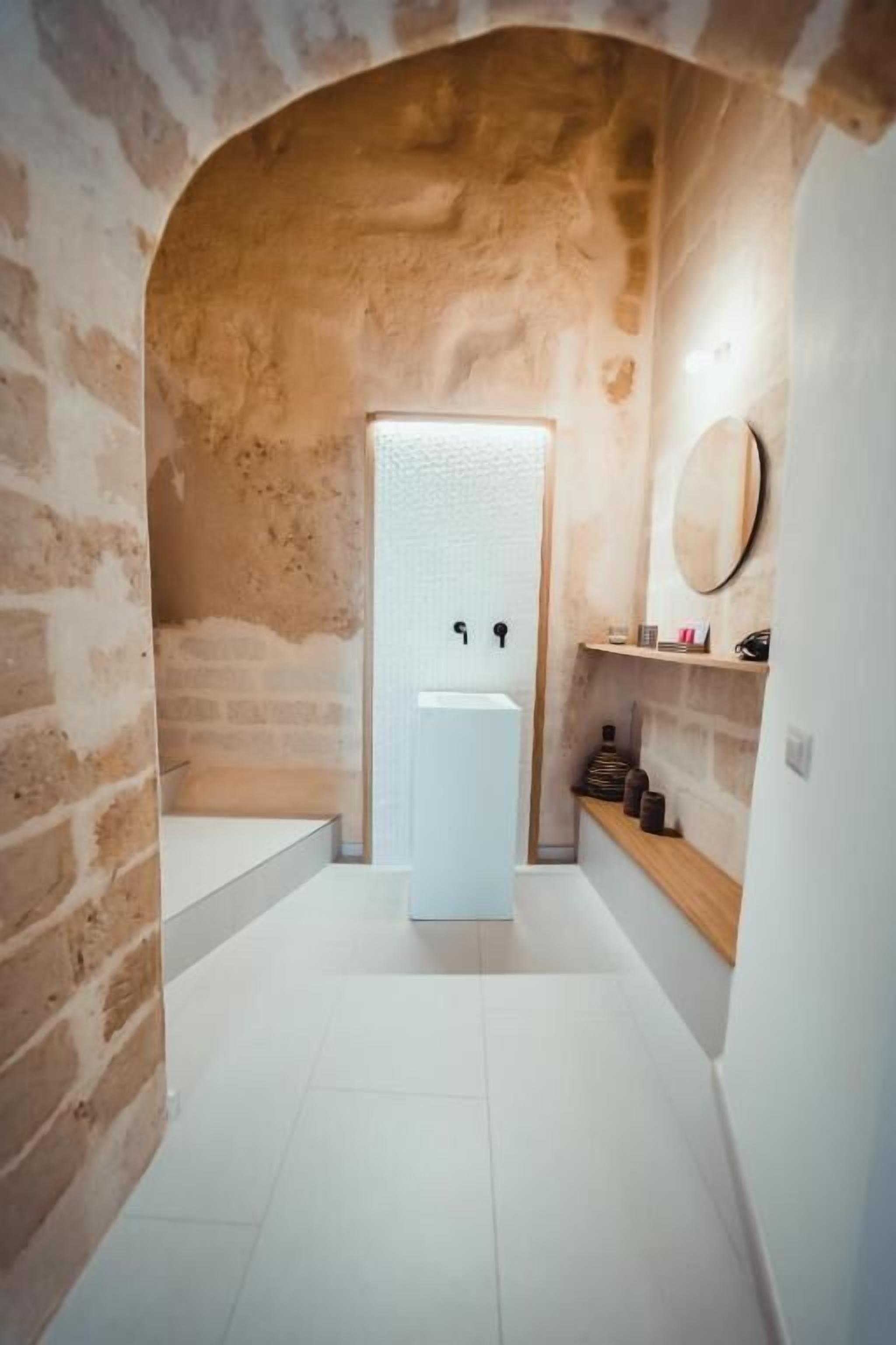 A bathroom with a white sink, a mirror, and a shelf with toiletries.