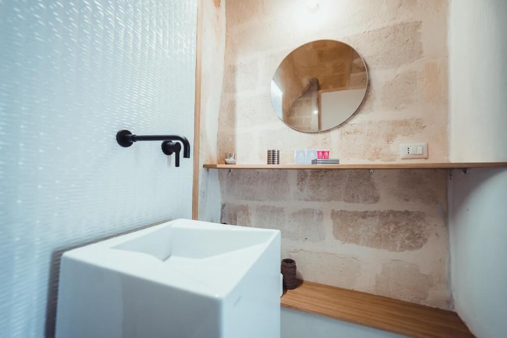 Une salle de bain avec un lavabo blanc, un miroir rond et une étagère en bois.