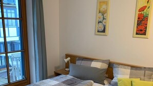 Een tweepersoonsbed met een sprei, twee kussens en opgevouwen handdoeken. Er hangen twee schilderijen aan de muur.